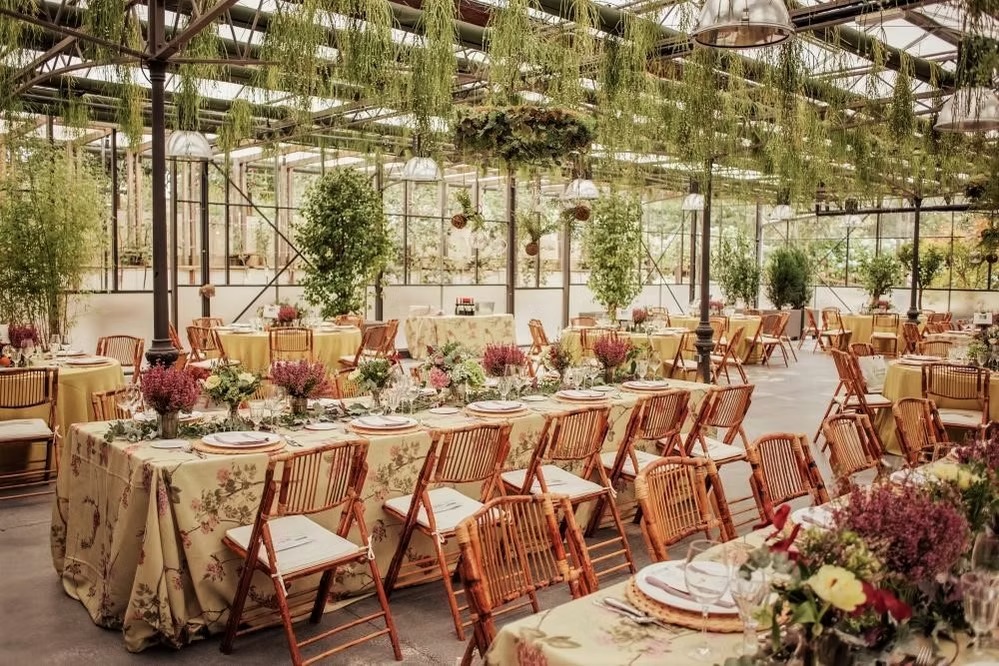 Montaje de evento con sillas de mimbre y mesas rectangulares bajo un invernadero